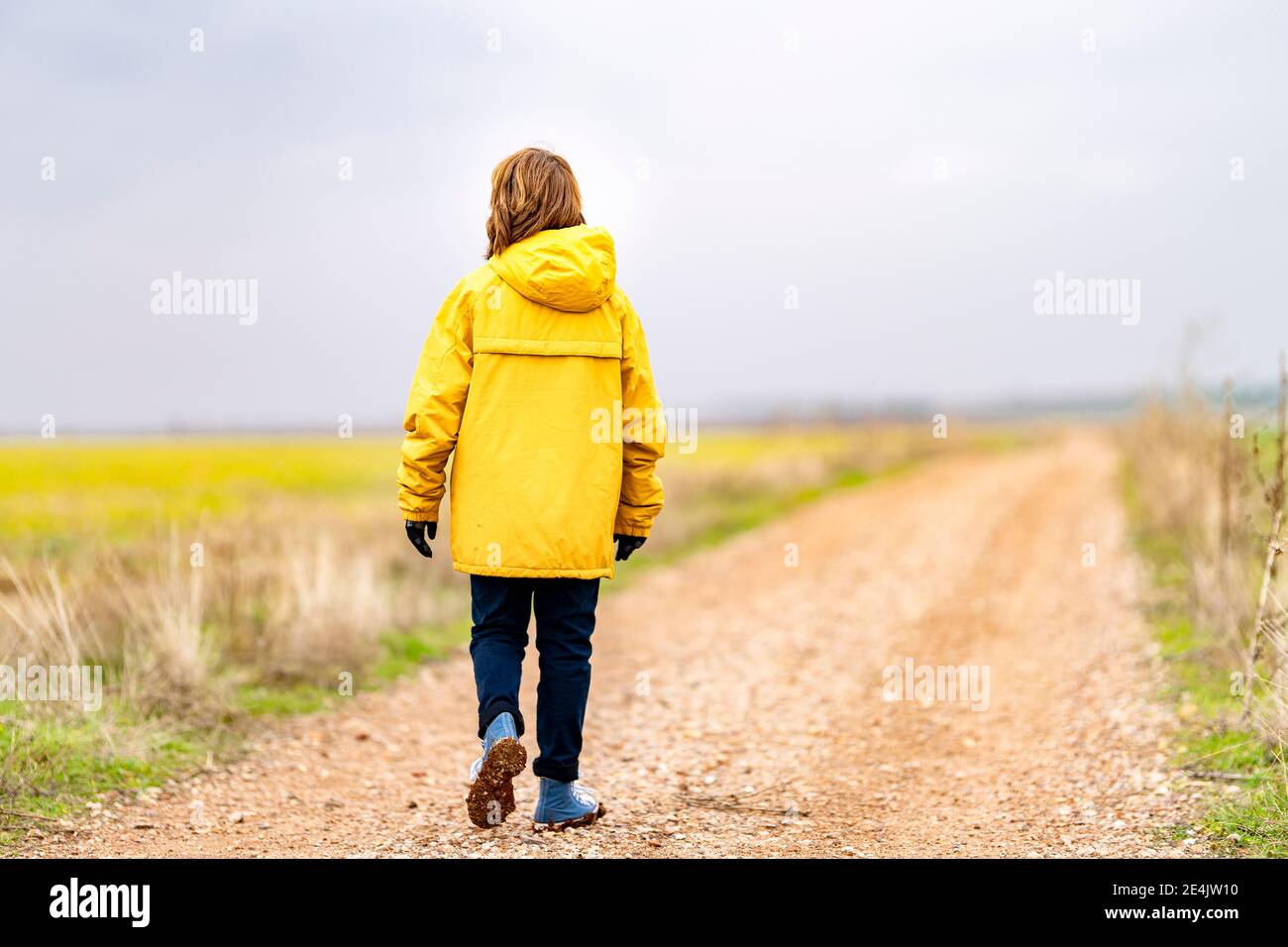 Ragazzo in giacca gialla che cammina lungo la strada sterrata vuota Foto Stock