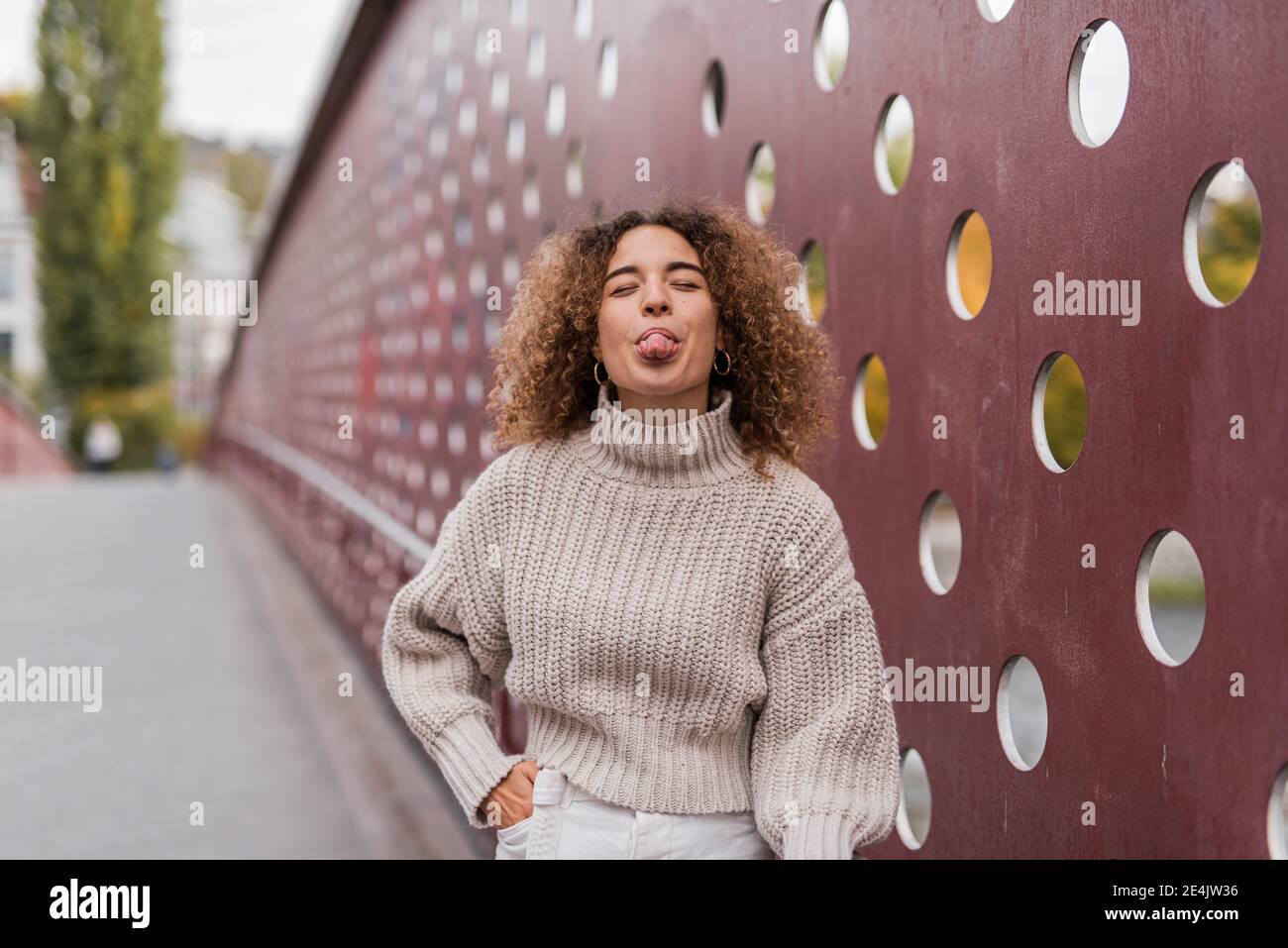 Giovane e giocosa donna afroica che si stacca dalla lingua mentre si alza contro il muro metallico Foto Stock