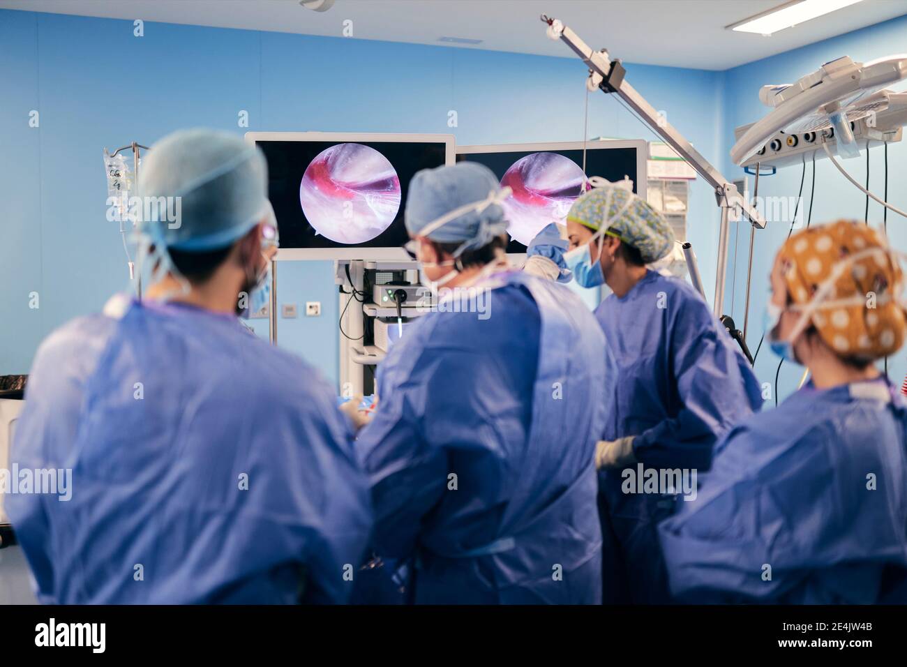 Medici che operano la chirurgia attraverso lo schermo del computer mentre si è in piedi al funzionamento camera durante COVID-19 Foto Stock