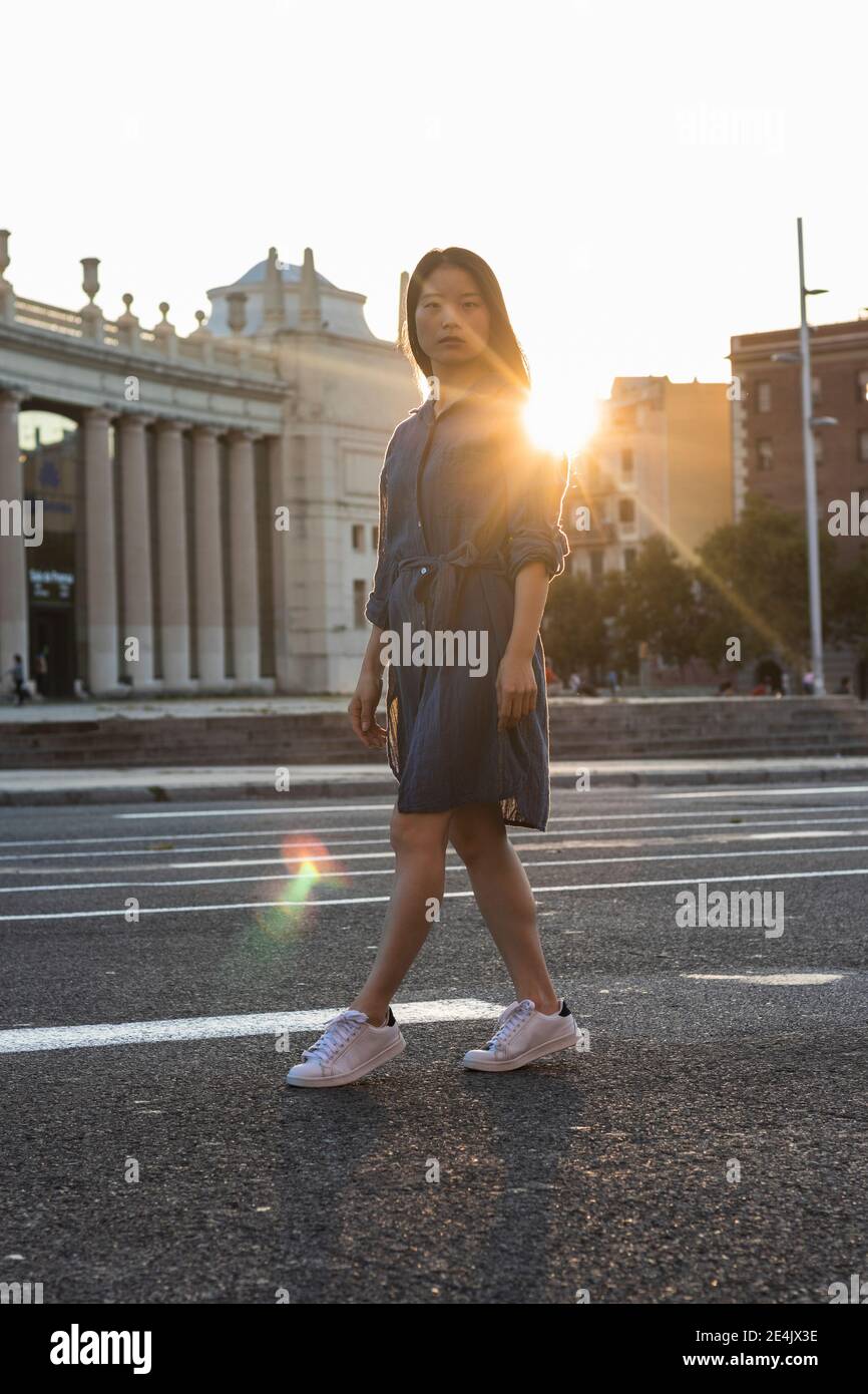 Donna che cammina per strada in città contro il cielo limpido durante tramonto Foto Stock