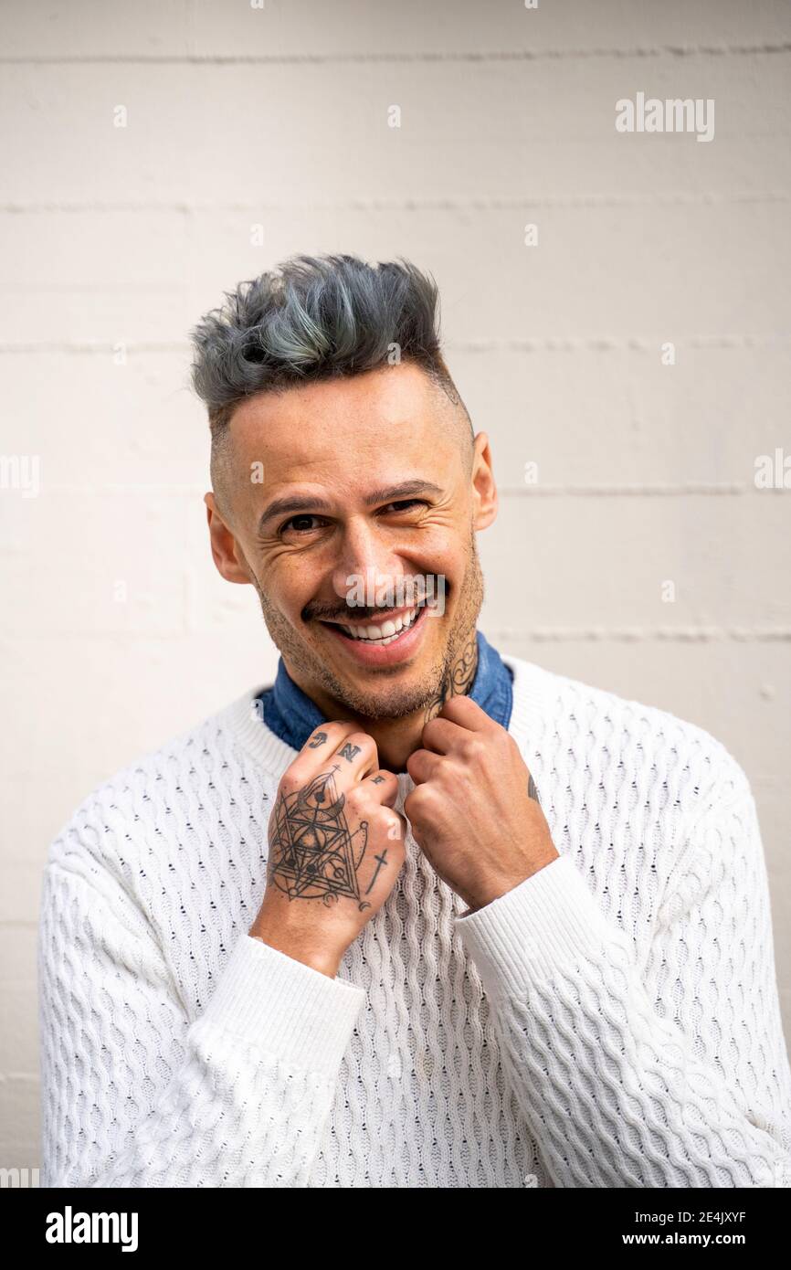 Uomo elegante e sorridente con tatuaggio contro la parete bianca Foto Stock