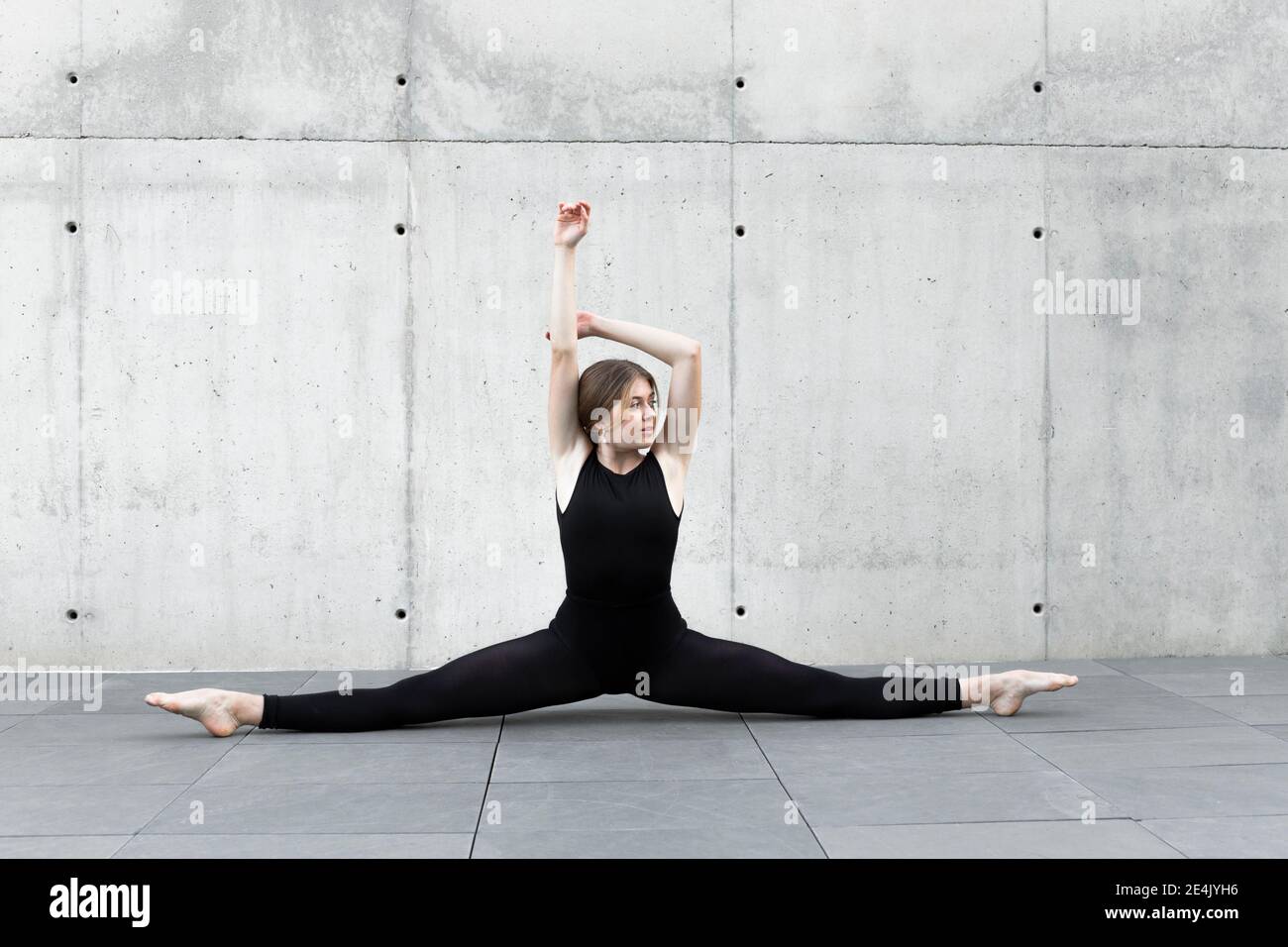 Ballerina in nero leotard facendo split di fronte al cemento parete Foto Stock