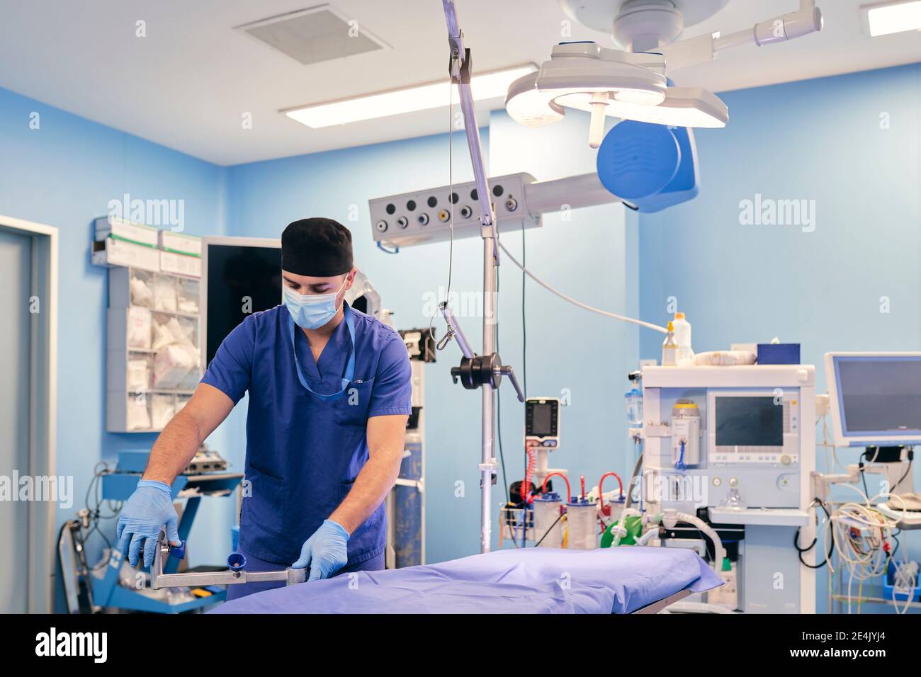 Assistente maschio che indossa la maschera facciale che regola il tavolo operatorio mentre si è in piedi in sala operatoria all'ospedale Foto Stock