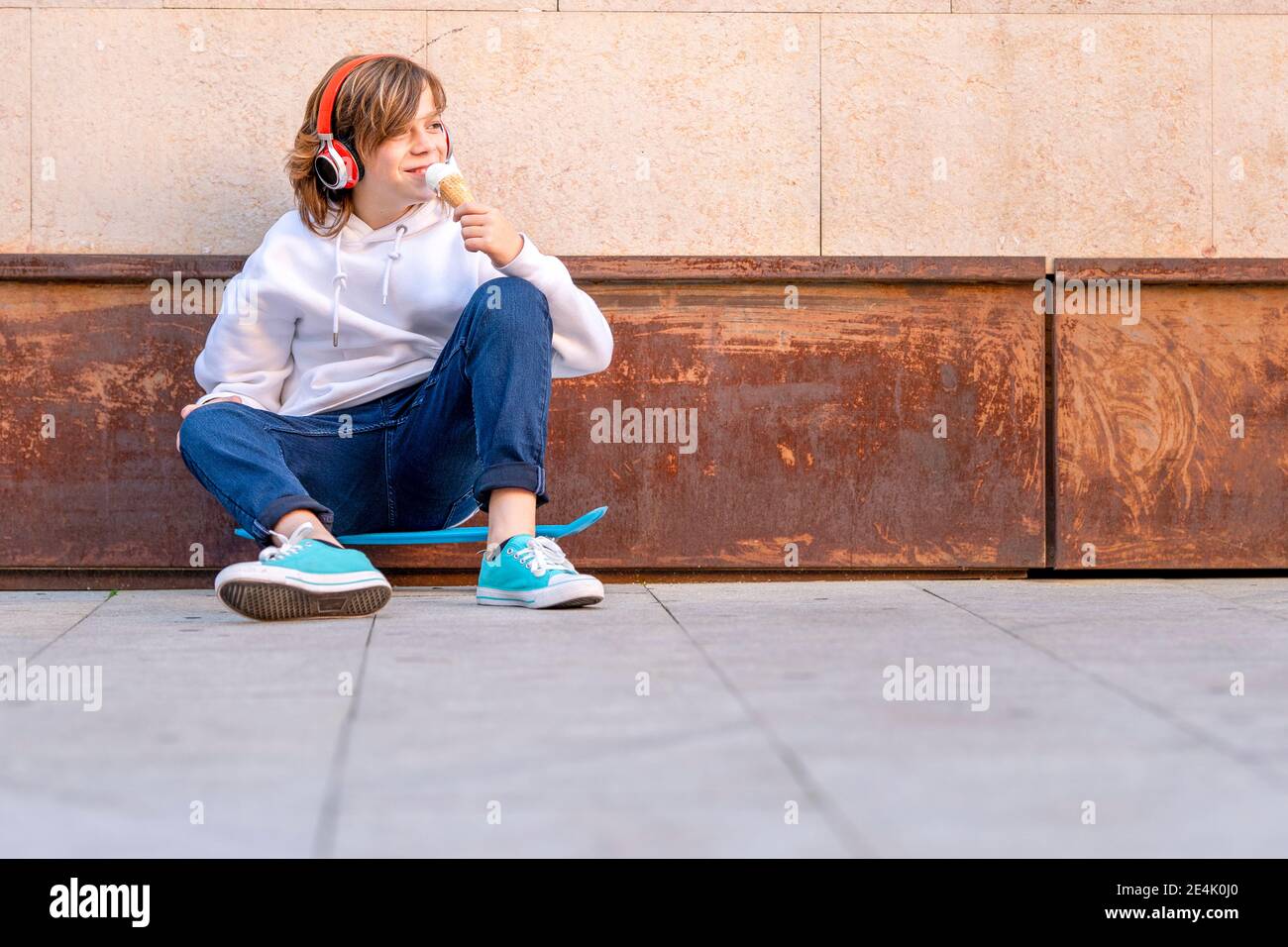 Ragazzo che indossa le cuffie mangiando gelato mentre si siede sul sentiero Foto Stock