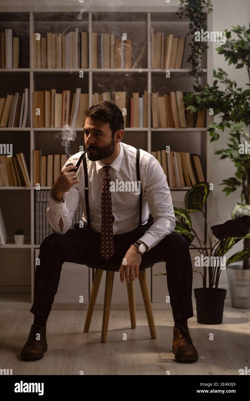 Ritratto di uomo bearded seduto su sgabello e fumo pipe Foto Stock