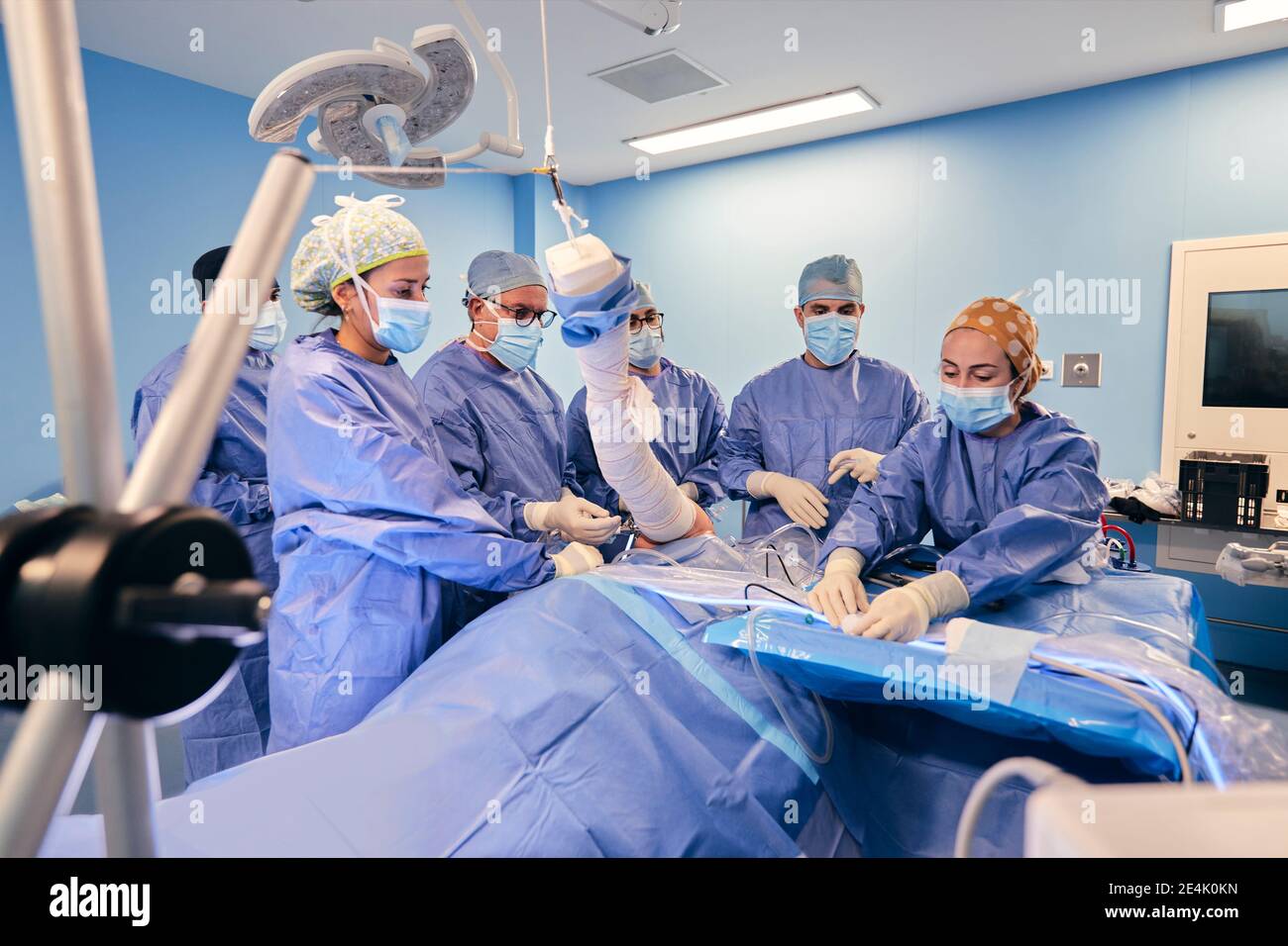 I medici che indossano la maschera di faccia che fa la chirurgia artroscopica del paziente mentre Stando in piedi al tavolo in sala operatoria durante il COVID-19 Foto Stock