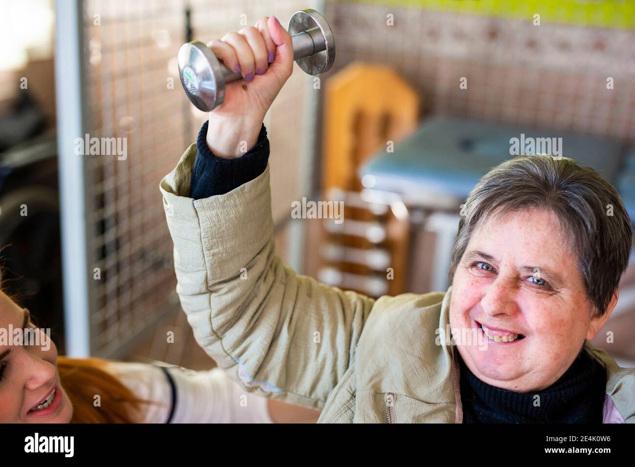 Sorridente donna disabile che fa esercizio di manubri con infermiere femmina in centro di riabilitazione Foto Stock