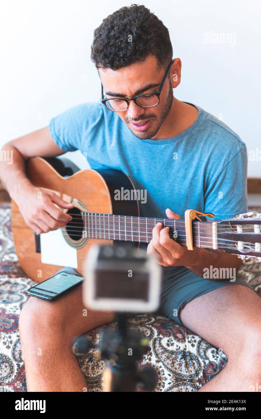 Musicista maschile che suona la chitarra per fare il video blog a casa Foto Stock