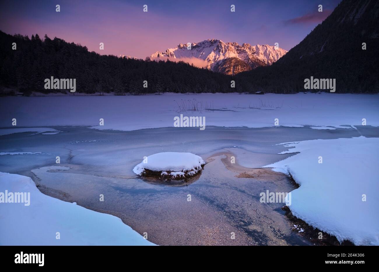 Ruscello che scorre su terra coperta di neve contro la montagna durante il tramonto Foto Stock