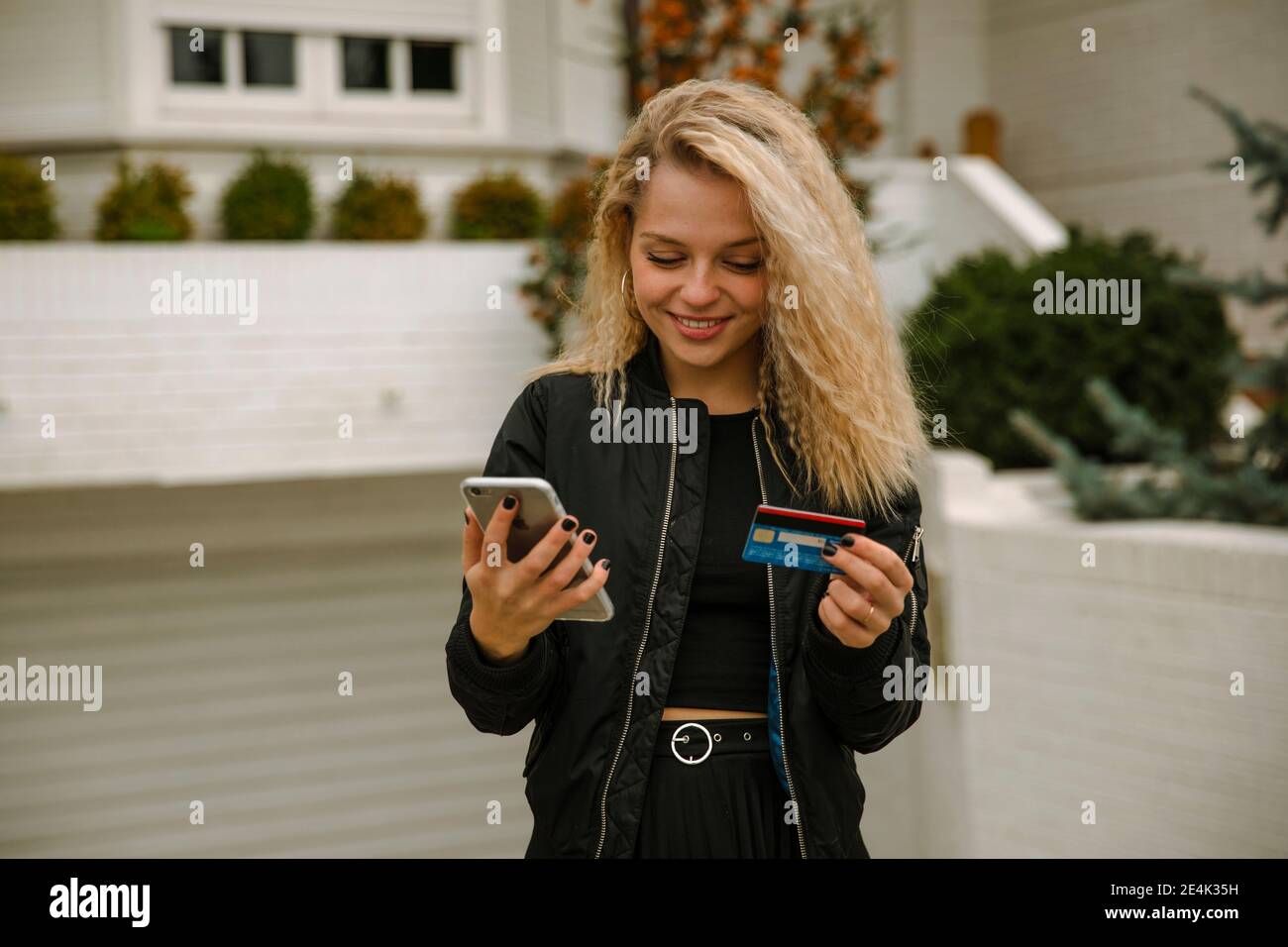 Donna bionda sorridente che acquista online tramite telefono cellulare e credito scheda Foto Stock