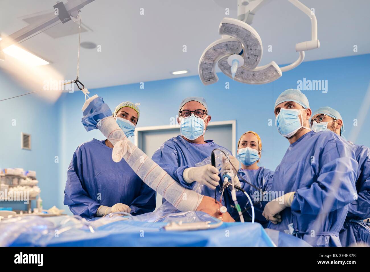 Chirurghi con maschera facciale che operano chirurgia artroscopica della spalla mentre si è in piedi In sala operatoria durante il COVID-19 Foto Stock
