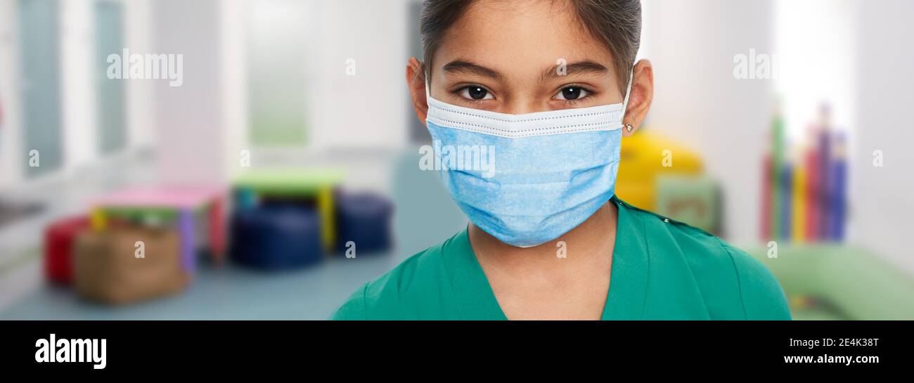 Bambina asiatica che indossa una maschera medica in piedi nel corridoio scolastico. Pandemia globale, quarantena a scuola Foto Stock