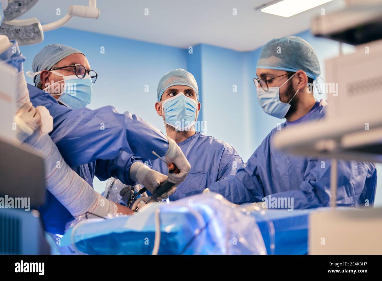 Medici di sesso maschile di chirurgia operatoria con attrezzature chirurgiche mentre si è in piedi Sala operatoria durante il COVID-19 Foto Stock