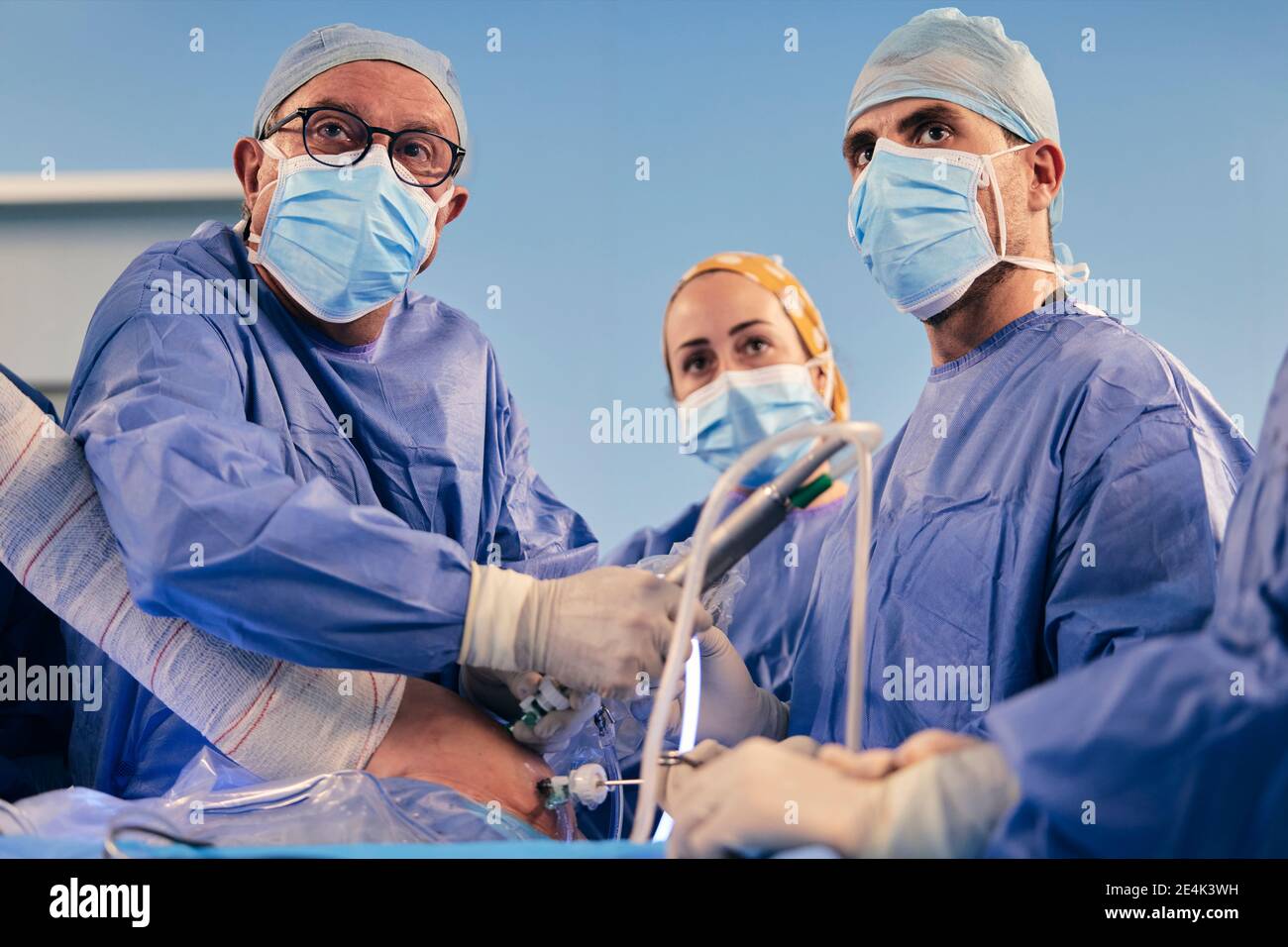 Chirurghi che indossano maschera protettiva faccia operando chirurgia artroscopica della spalla mentre In piedi nella sala operatoria durante il COVID-19 Foto Stock