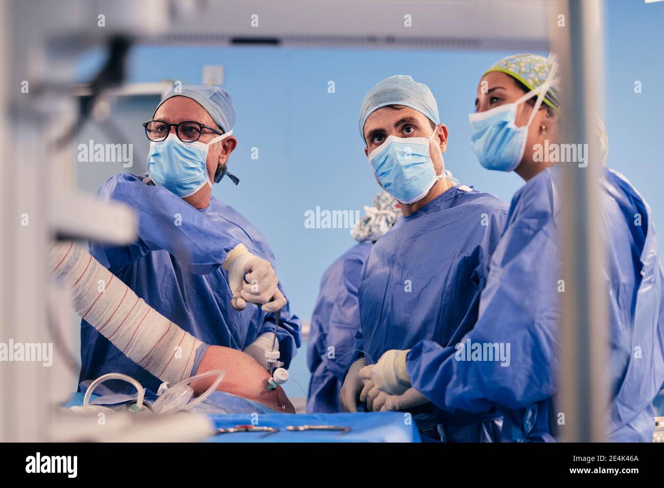 Squadra di chirurgo che indossa la maschera protettiva della faccia che opera chirurgia artroscopica della spalla in piedi nella sala operatoria Foto Stock