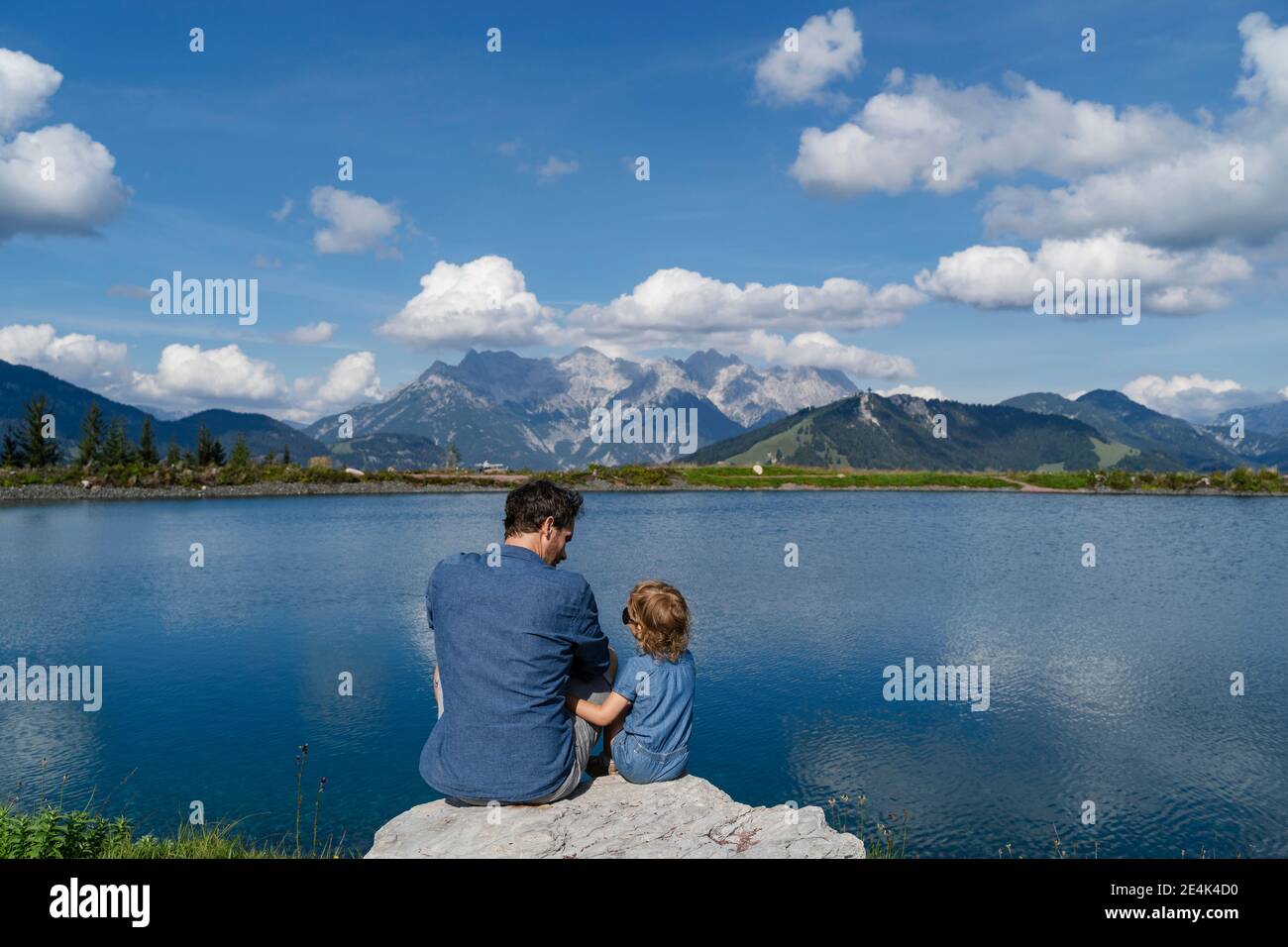 Padre e piccola figlia seduti insieme sulla riva del lago boulder Foto Stock