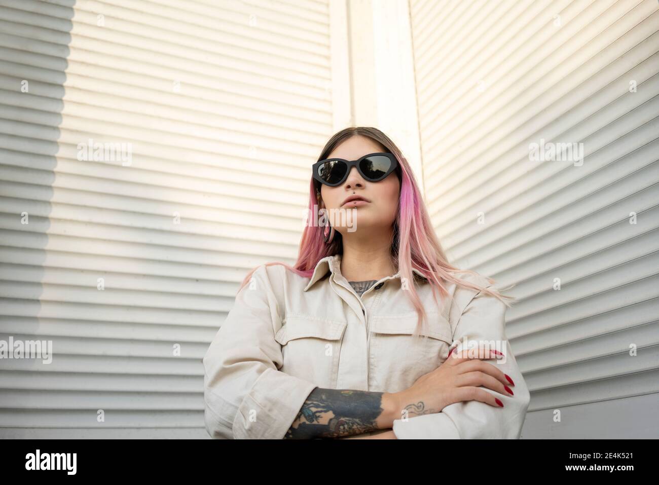 Donna alla moda con le braccia incrociate in occhiali da sole contro  texture bianca parete Foto stock - Alamy