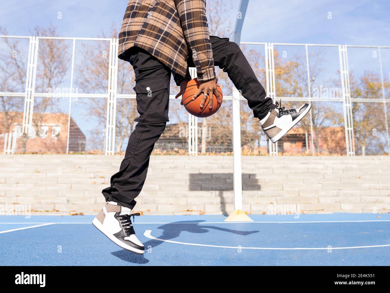 Giovane uomo che gioca palla basket in campo sportivo al sole giorno Foto Stock