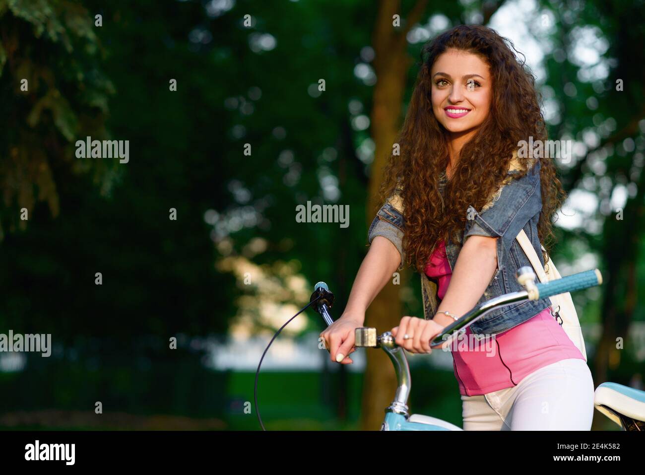 Gioiosa giovane donna in bicicletta nel parco verde al tramonto Foto Stock