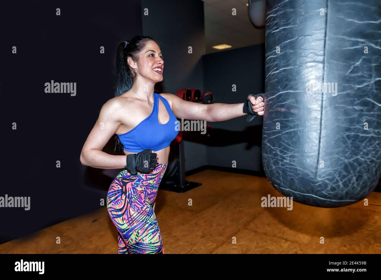 Sorridente bella donna che si esercita con la borsa da punzonatura in palestra Foto Stock