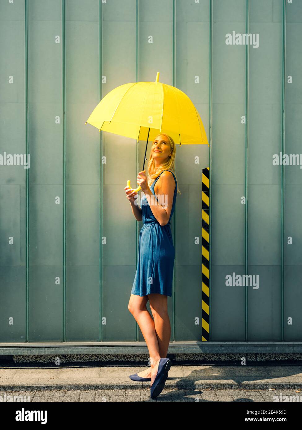 Giovane donna con ombrello sul sentiero contro il muro durante il sole giorno Foto Stock