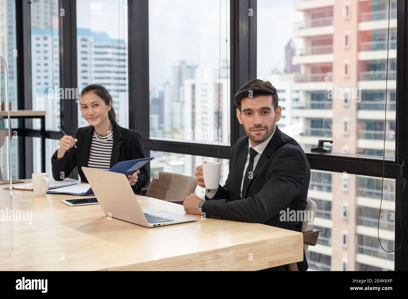 Uomo esecutivo caucasico che tiene la tazza di caffè e donna segretaria che prende nota del documento aziendale in un ufficio moderno nel quartiere degli affari Foto Stock