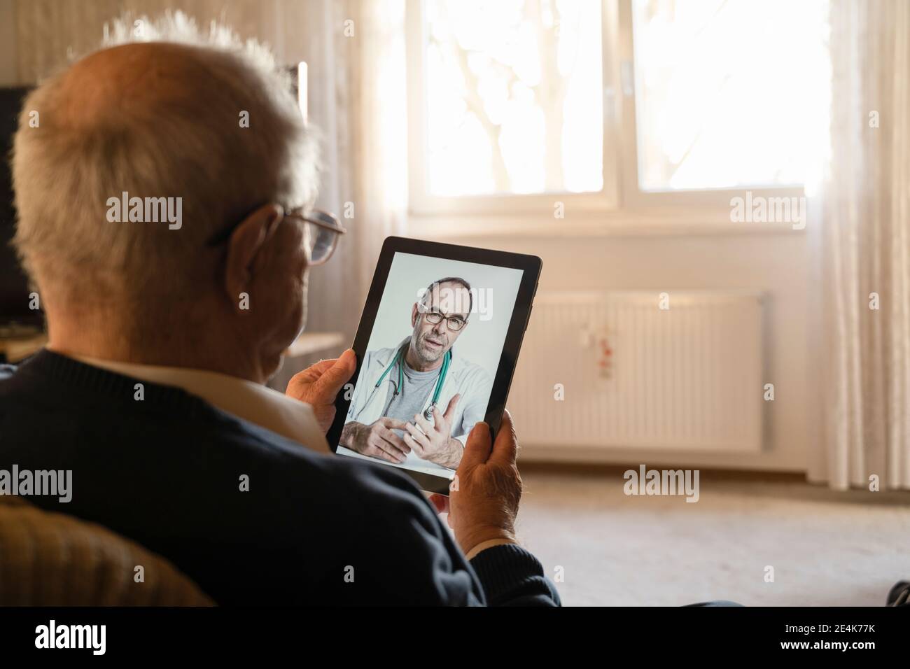 Medico generico che consulta l'uomo anziano online attraverso il tablet digitale in soggiorno Foto Stock