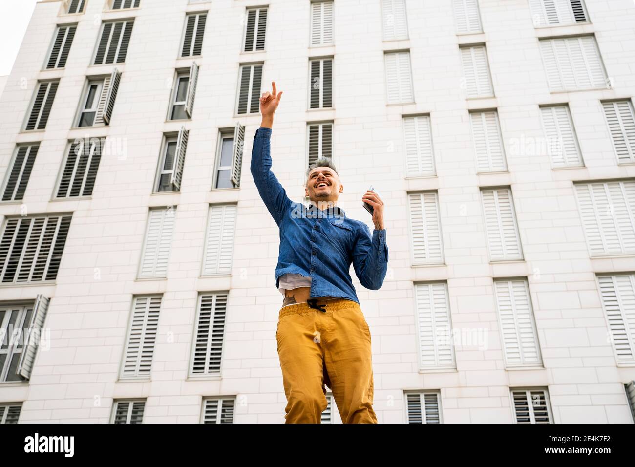 Uomo allegro che salta con la mano sollevata contro l'edificio bianco Foto Stock