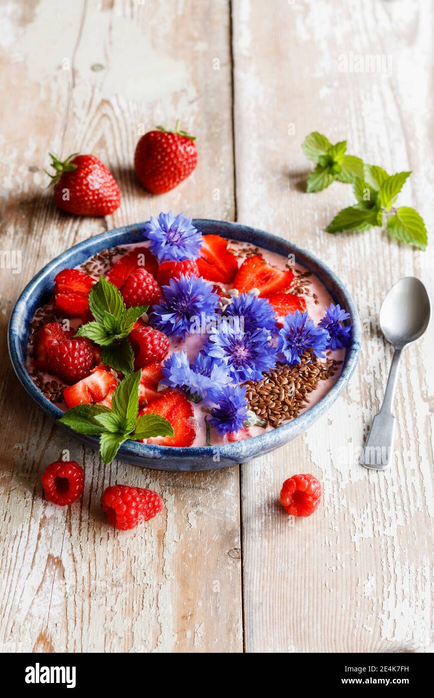 Piatto di yogurt con lamponi, fragole, fiori di mais e menta Foto Stock