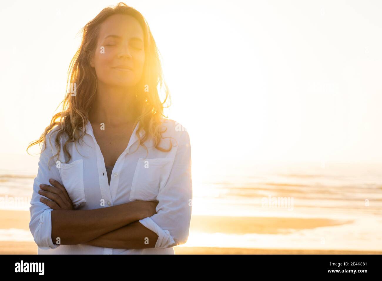 Donna in piedi con gli occhi incrociati in spiaggia durante il tramonto Foto Stock