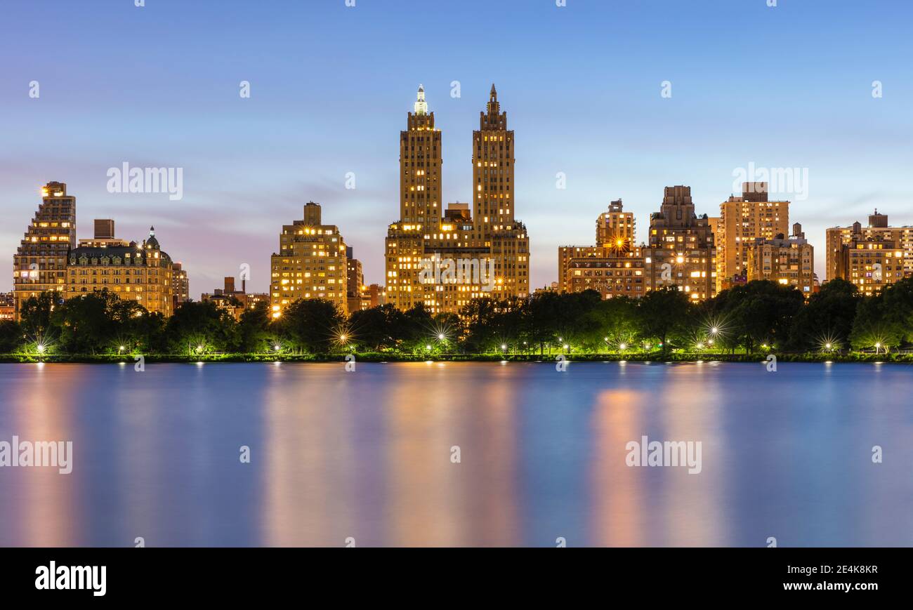 Stati Uniti, New York, New York City, Upper West Side edifici illuminati al crepuscolo visto attraverso Jacqueline Kennedy Onassis Reservoir Foto Stock