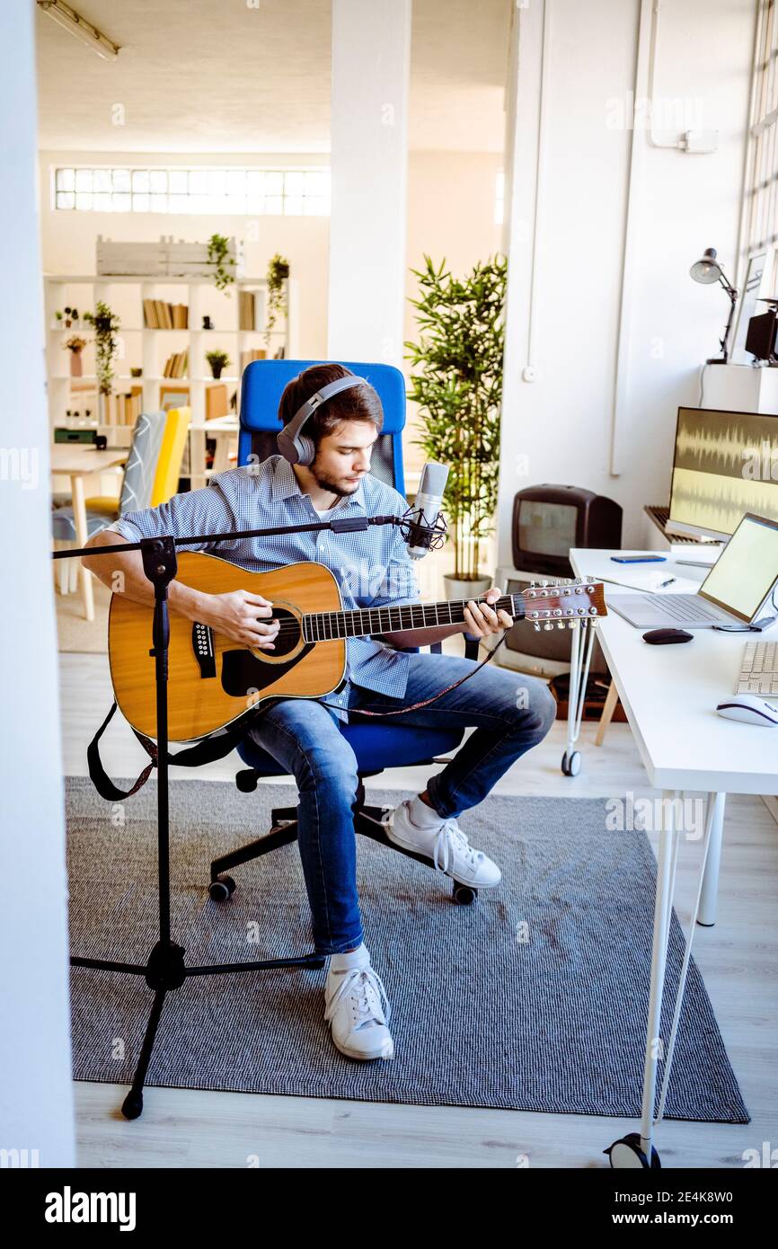 Musicista con microfono che suona la chitarra mentre si siede nello studio di registrazione Foto Stock