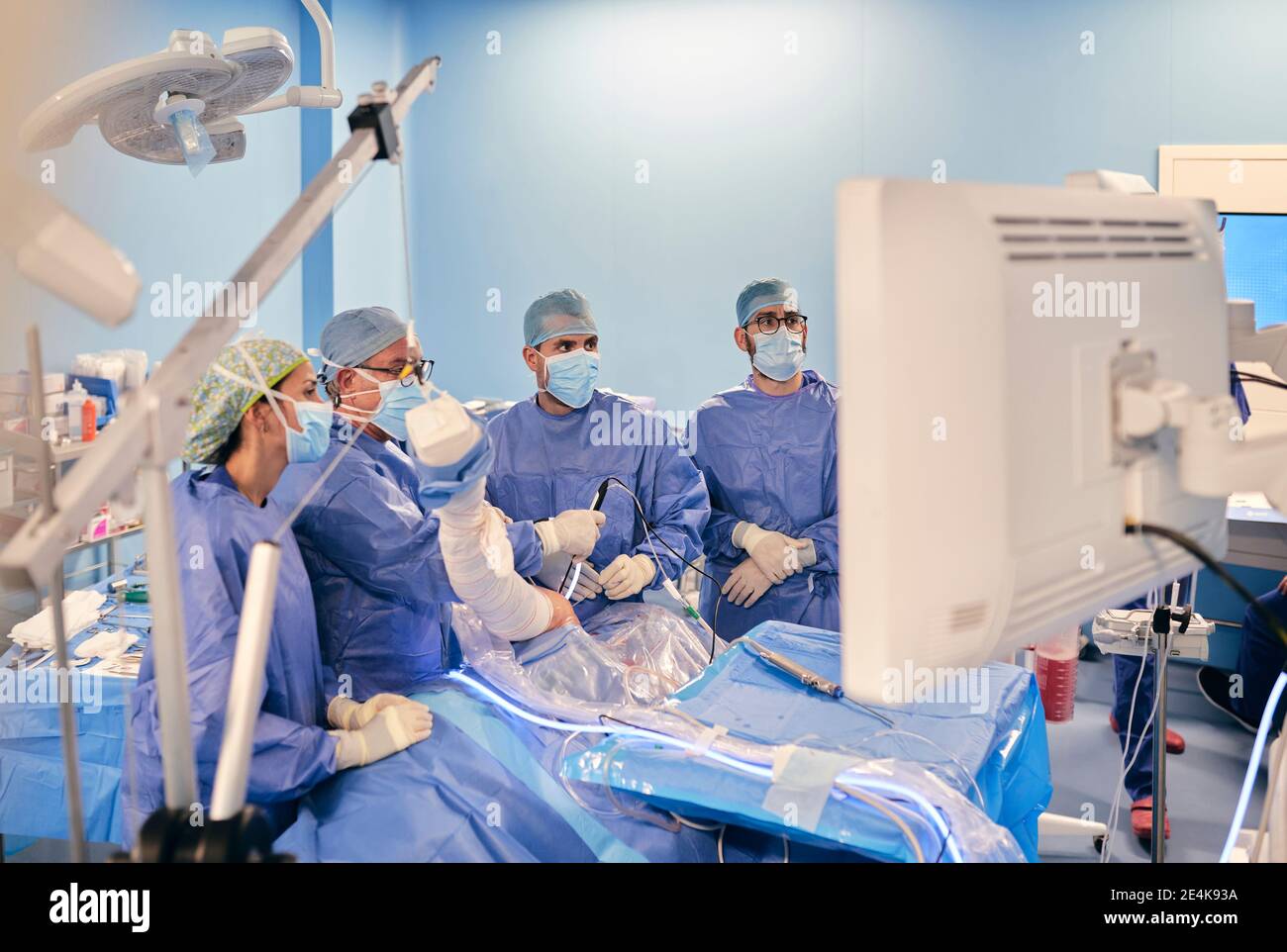 Chirurghi in maschera facciale e scrub medici che operano chirurgia artroscopica In piedi nella sala operatoria durante il COVID-19 Foto Stock