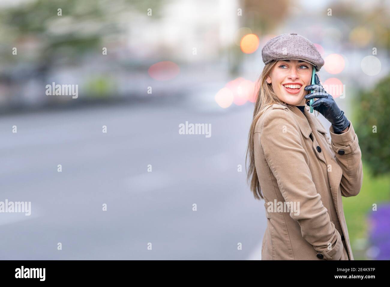 Donna sorridente e attraente che parla su smartphone in piedi per strada Foto Stock