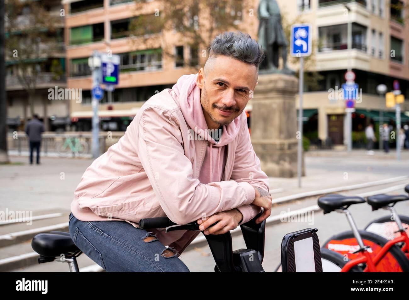 Elegante uomo medio adulto seduto in bicicletta contro l'edificio in città Foto Stock
