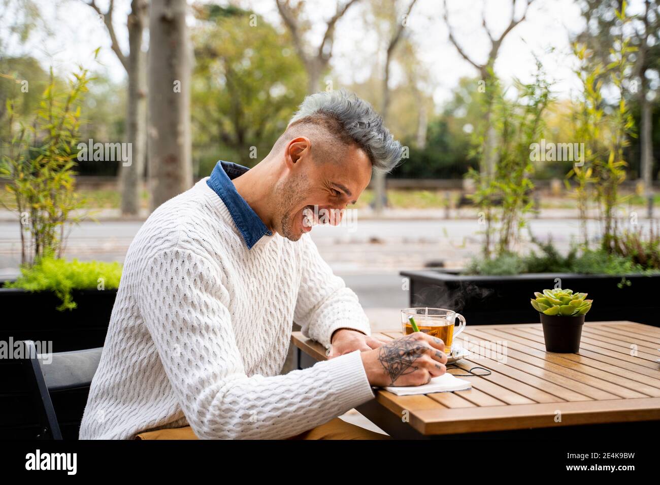Uomo felice che scrive nel libro mentre prendendo la pausa del tè dentro caffè Foto Stock