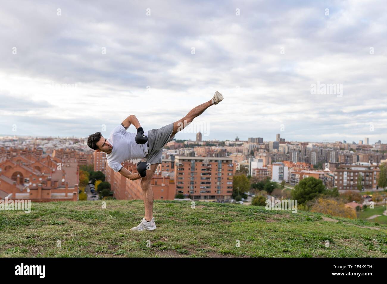 maschio acrobat praticare kickboxing contro cielo nuvoloso sulla città Foto Stock