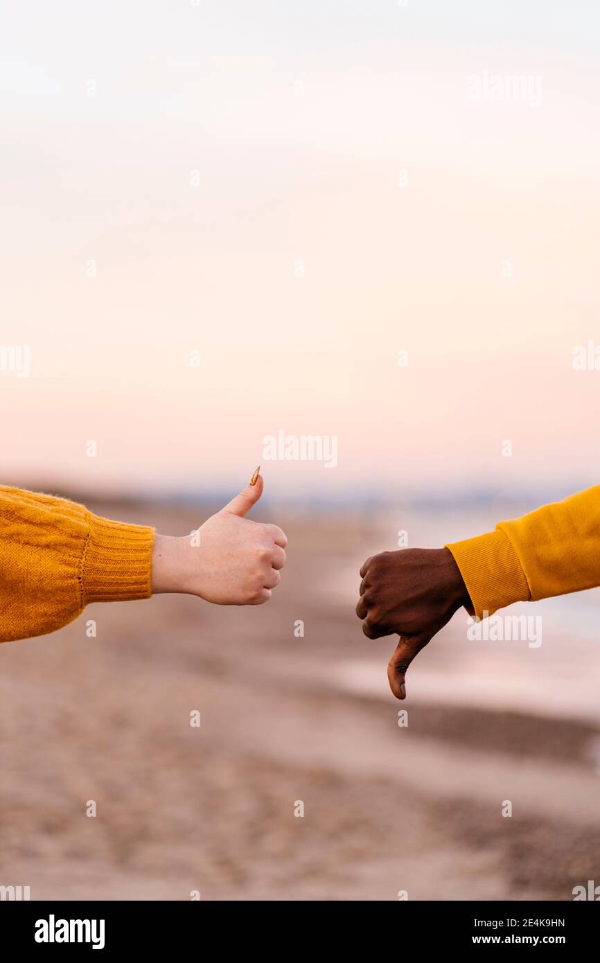 Coppia che mostra i pollici verso l'alto e verso il basso gesto in spiaggia Foto Stock