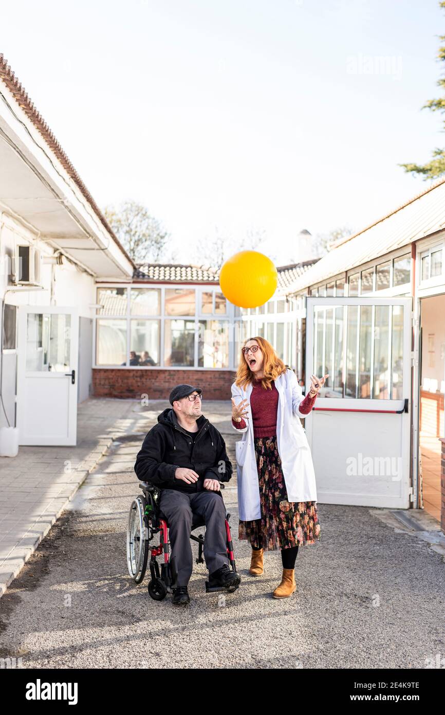 Infermiera femminile e uomo disabile che gioca con la palla contro il cielo fuori casa di cura Foto Stock