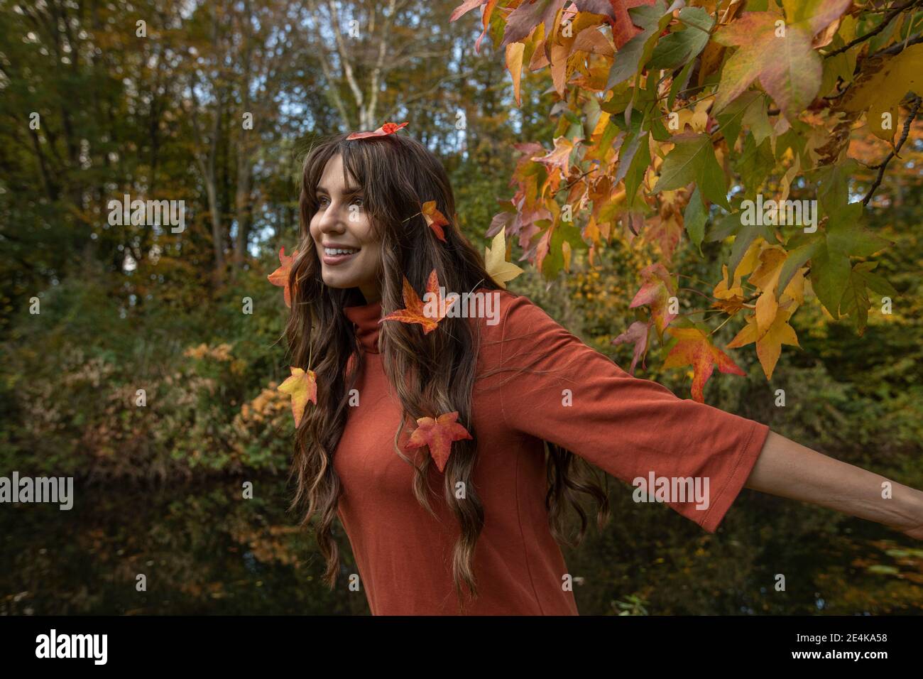 Donna felice con foglie autunnali in capelli che guardano via parco pubblico Foto Stock