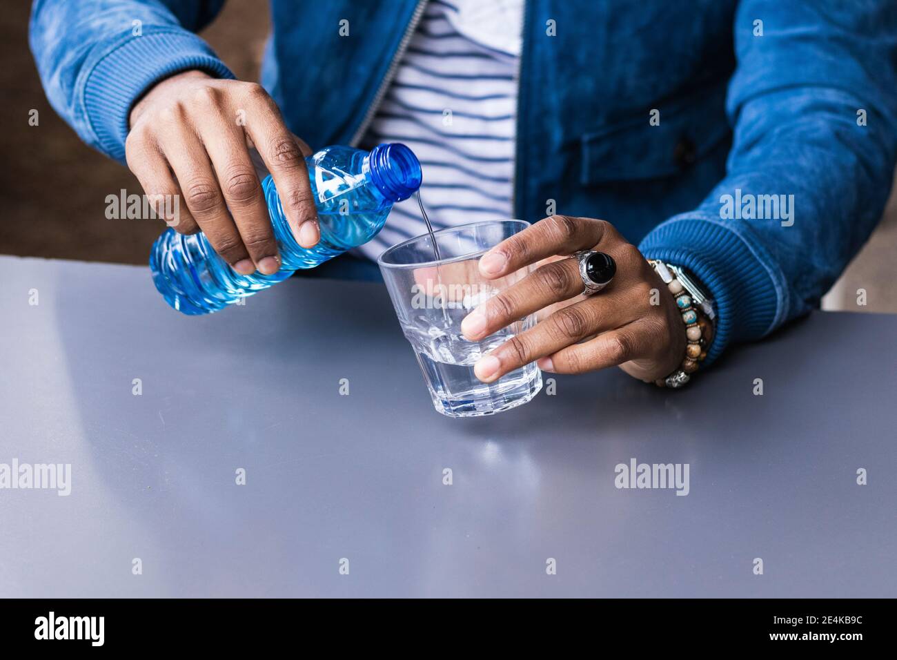 Primo piano di un uomo medio adulto che versa acqua in vetro sopra tavolo al bar sul marciapiede Foto Stock