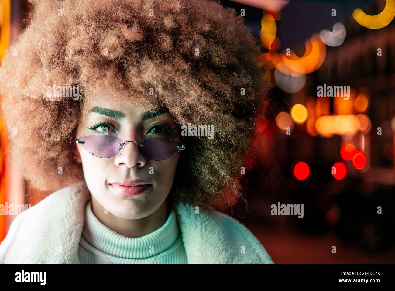 Primo piano di una donna elegante con capelli afro che indossa occhiali da sole città illuminata di notte Foto Stock