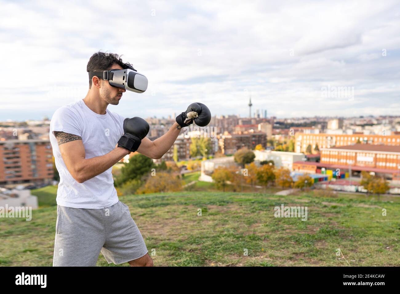 Acrobat maschio indossando una cuffia per realtà virtuale che pratica la boxe in collina in città Foto Stock