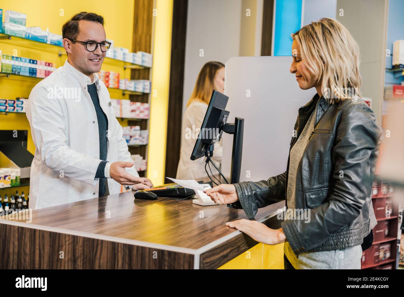 Cliente sorridente che dà la prescrizione al venditore nel negozio chimico Foto Stock