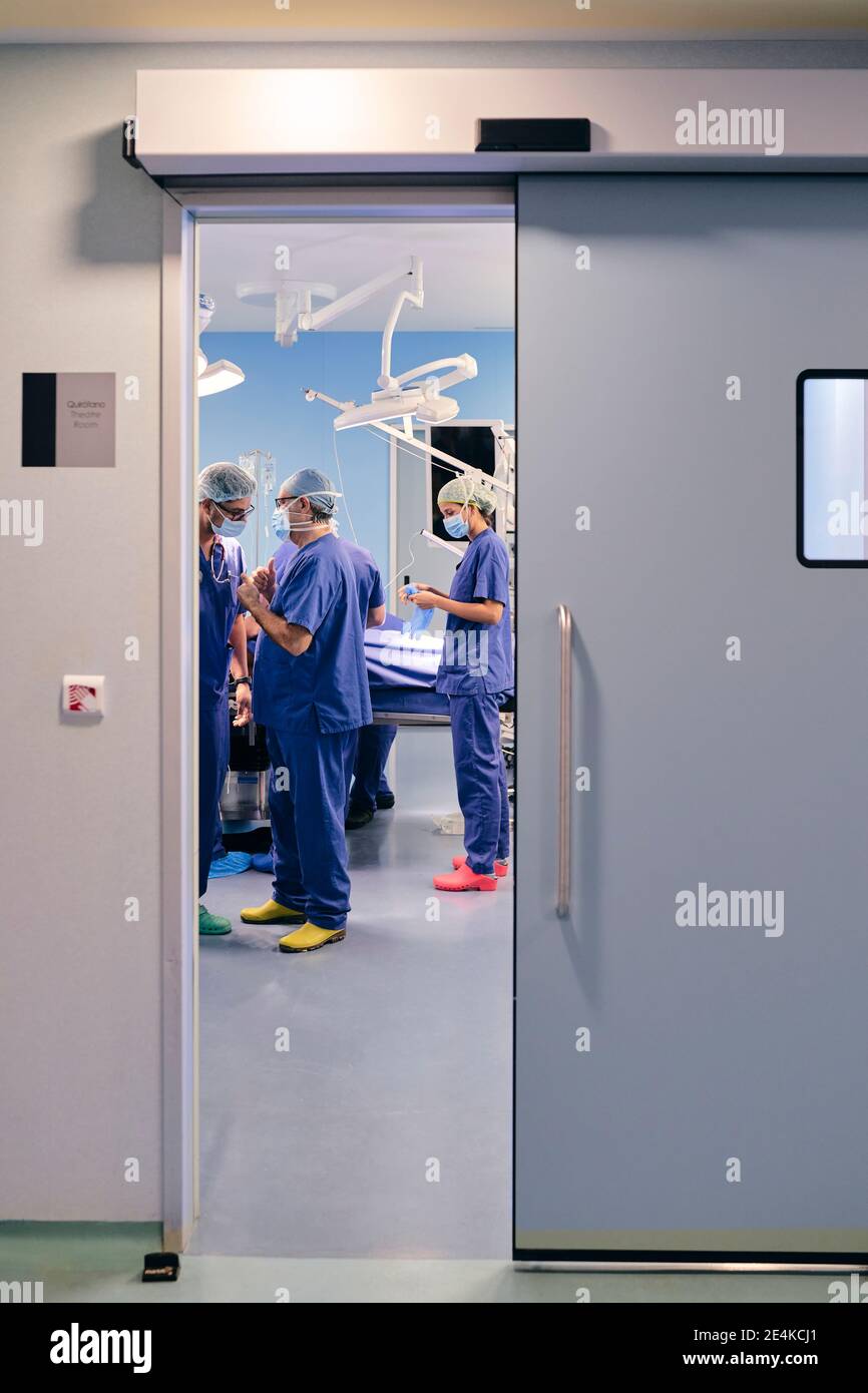 I medici che indossano la maschera di faccia che hanno discussione mentre si levano in piedi in funzione camera in ospedale Foto Stock