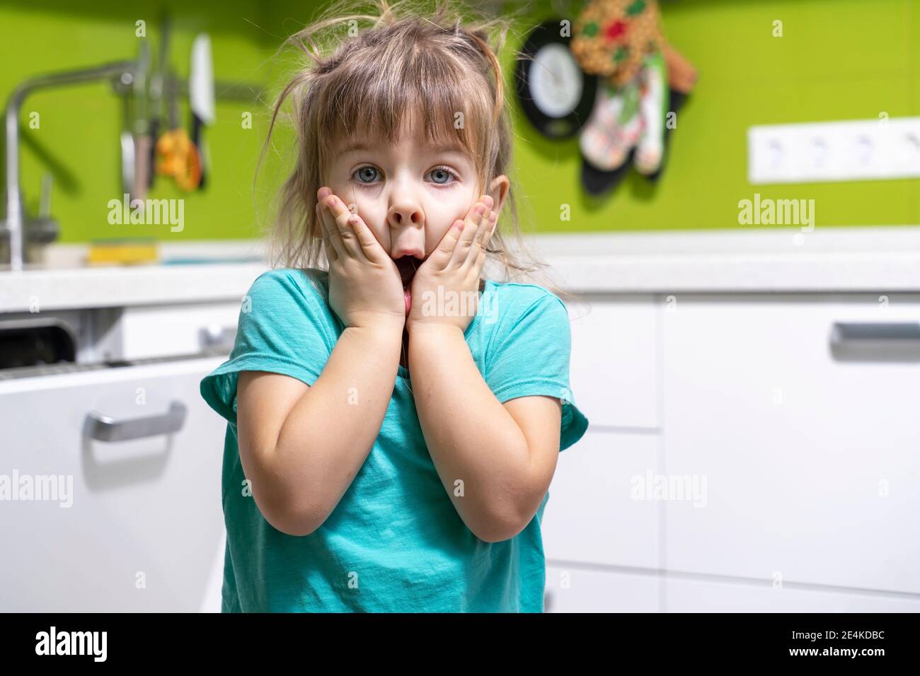 la bambina emozionale con capelli scoscesi è in shock. il bambino ha stretto il viso temendo caos in cucina Foto Stock