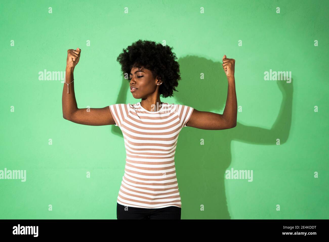 Giovane donna con gli occhi chiusi mostrando pugno mentre si sta in piedi contro sfondo verde Foto Stock