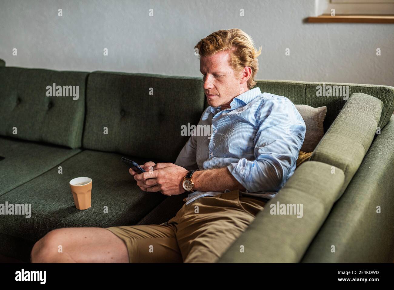 Messaggi di testo uomo per adulti di mezza età sullo smartphone mentre si è sdraiati sul divano in soggiorno Foto Stock