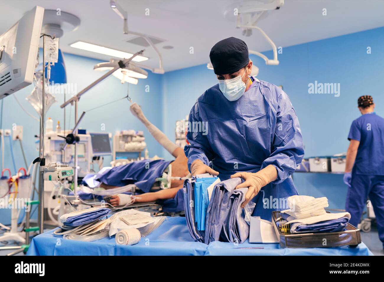 Medico indossando maschera viso scegliere abiti mentre si è in piedi con il collega nella sala operatoria Foto Stock