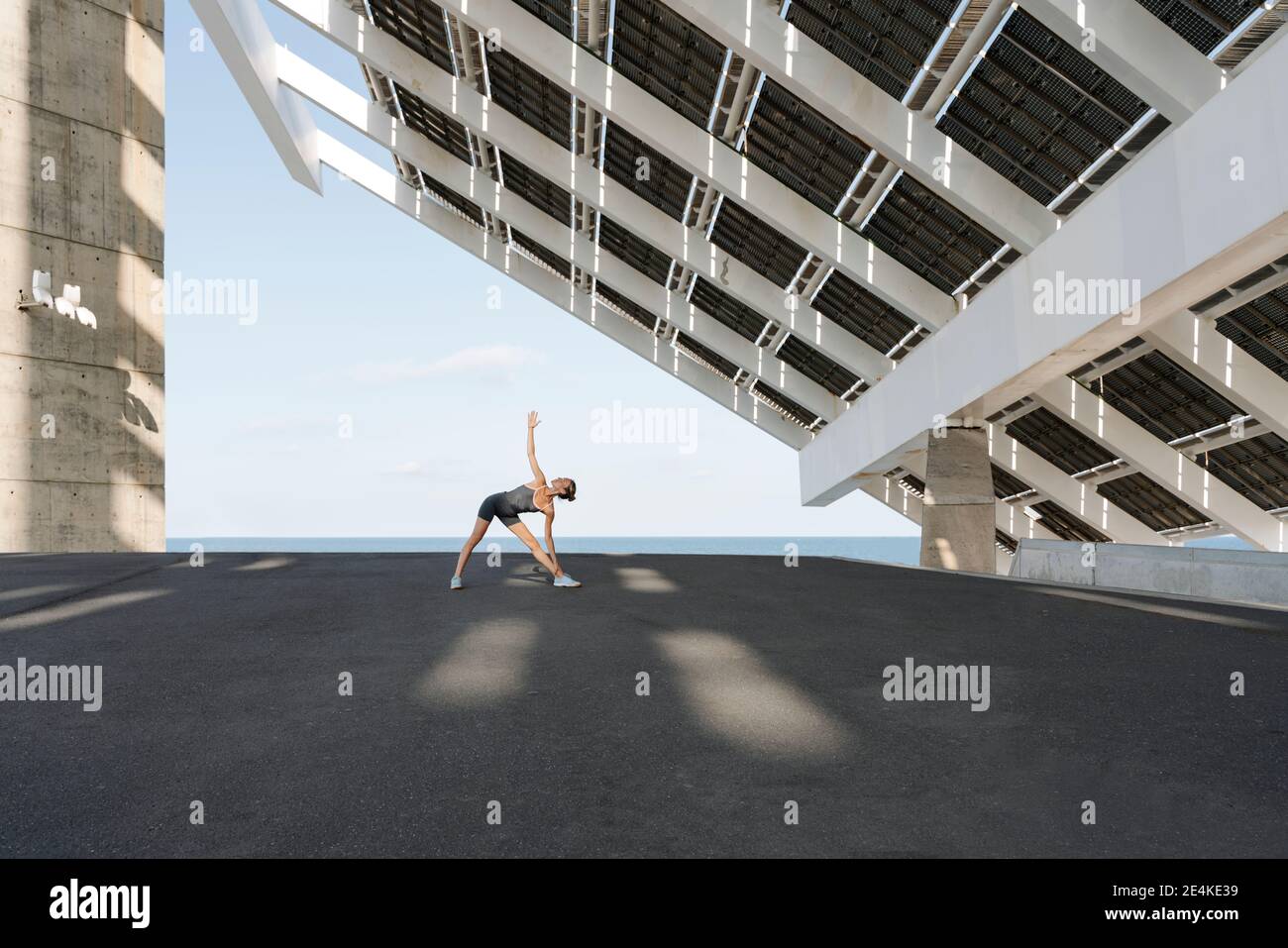 Sportiva con mano sollevata praticare yoga sotto struttura costruita contro cielo Foto Stock